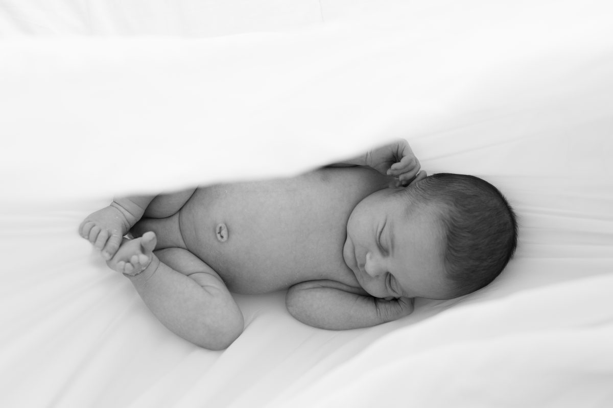 Nouveau-né photographié sous un voile blanc en noir et blanc